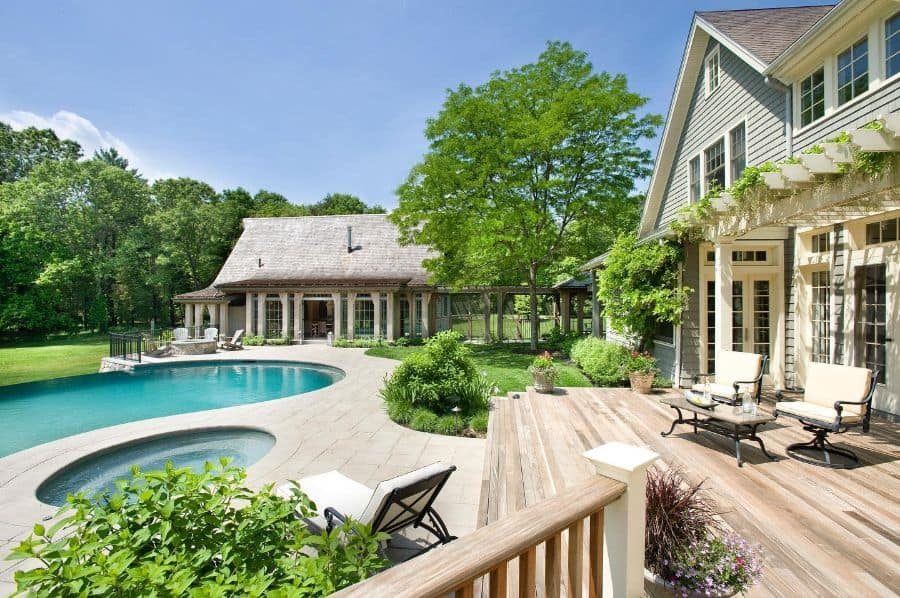 Elegant countryside pool house with a thatched roof, a serene curved pool, and a lush landscaped garden, creating a luxurious outdoor retreat