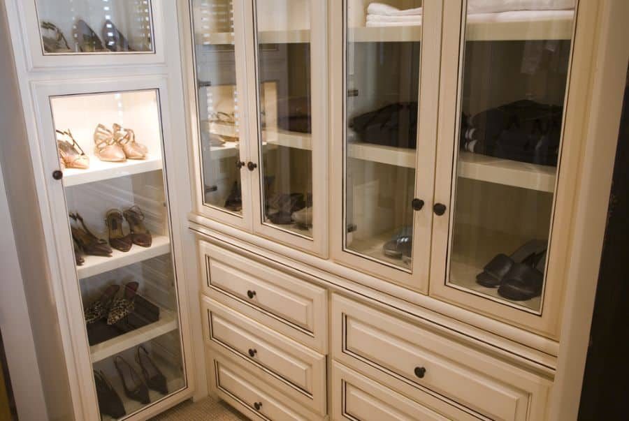 Walk-in closet with white cabinetry, displaying shoes on glass shelves, including sandals and heels, drawers below for additional storage