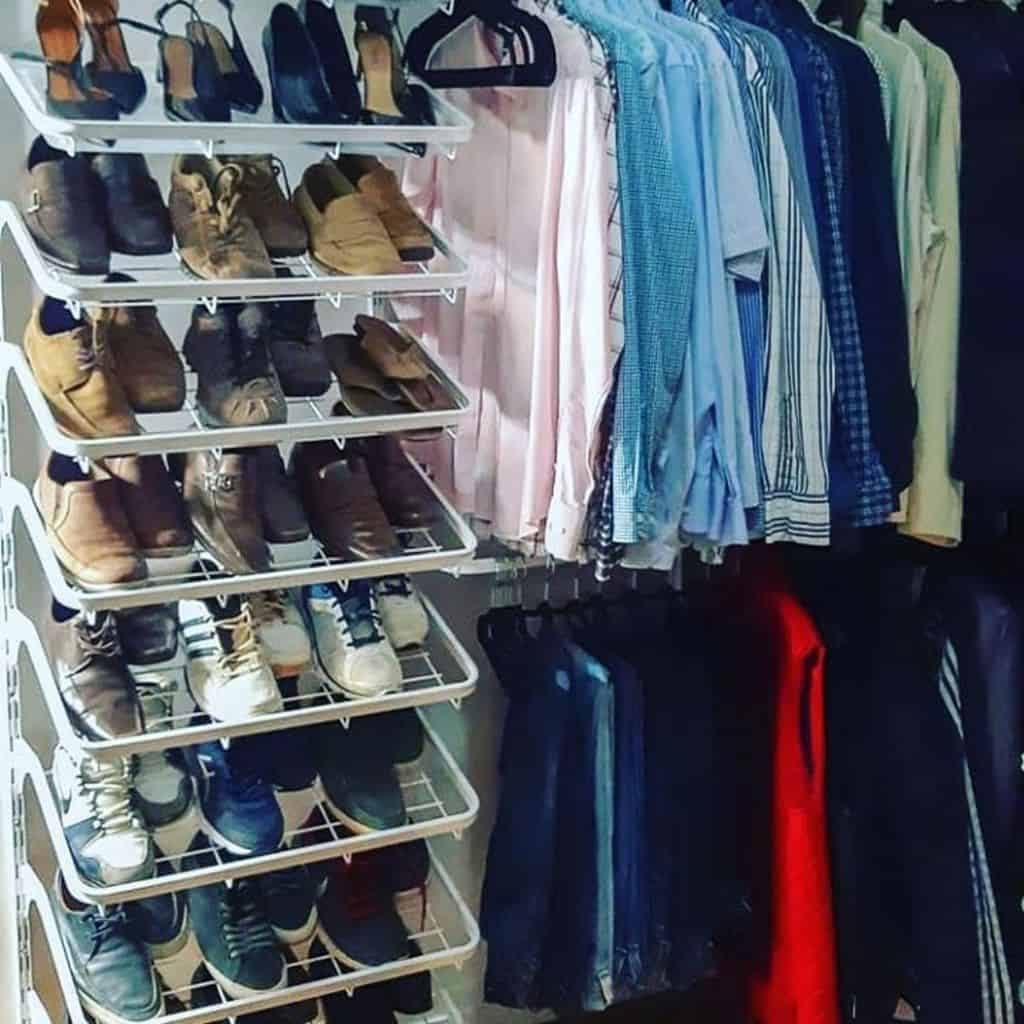 A closet with neatly organized shoes on racks and shirts hanging on hangers