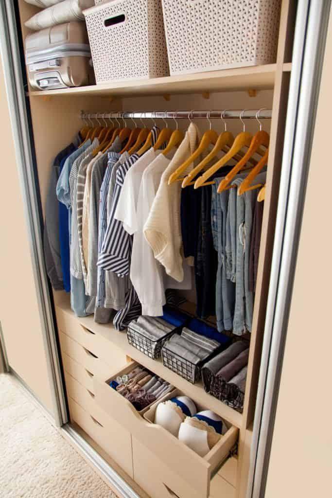 Organized closet with neatly hung clothes, folded jeans, and baskets on shelves; drawers hold neatly arranged socks and items