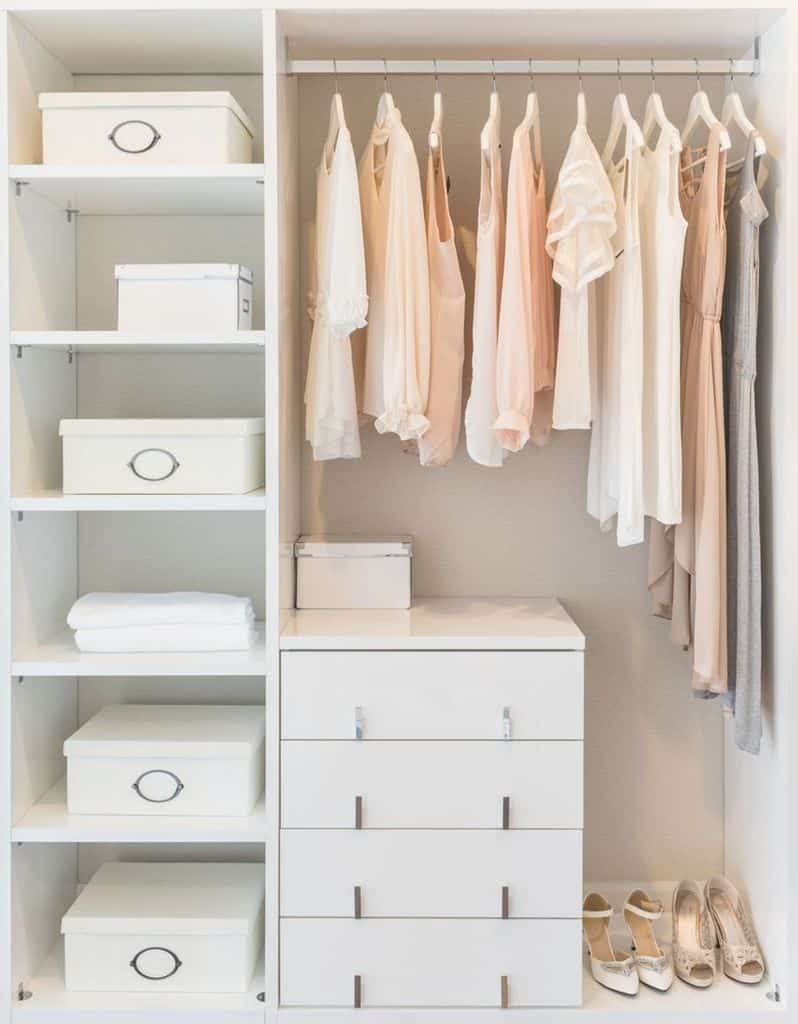 Minimalist white wardrobe with neatly hung clothes, boxes, and shoes on display, emphasizing organization and light colors