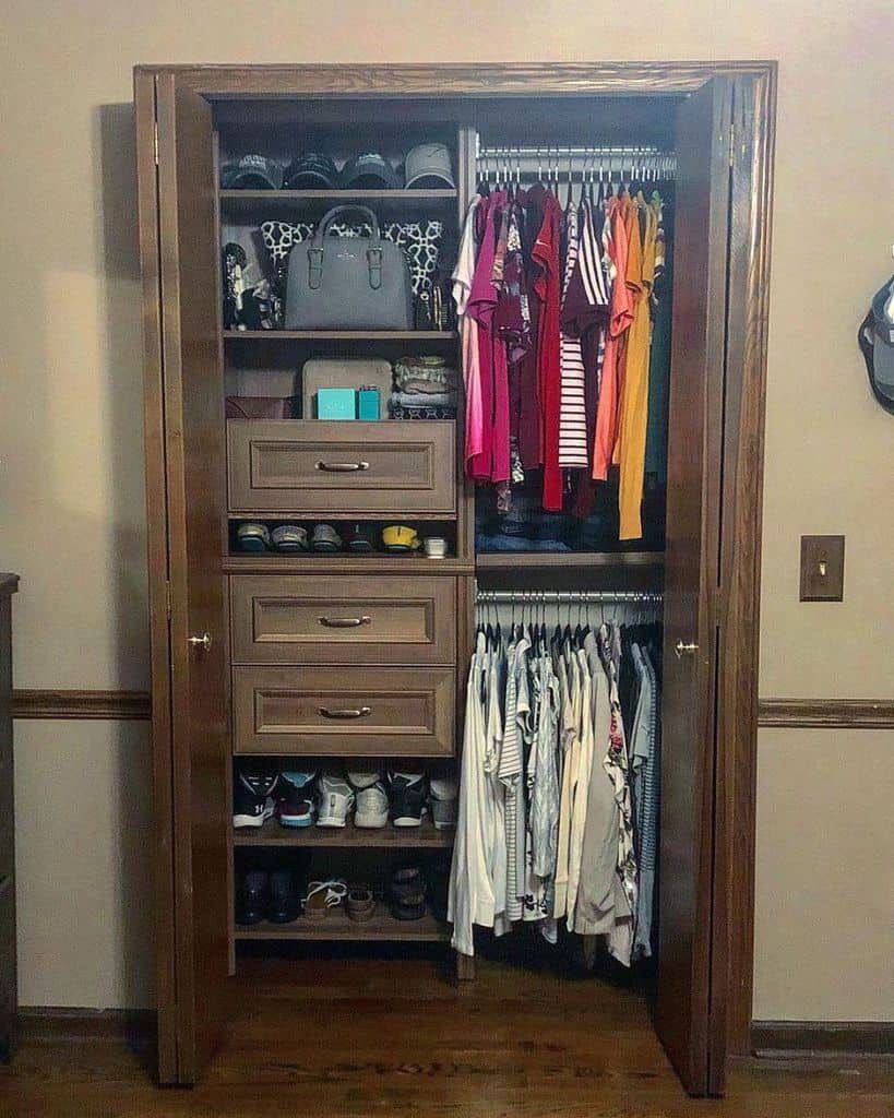 A neatly organized closet with clothes hung on both sides, shoes and bags on shelves, and three drawers in the center