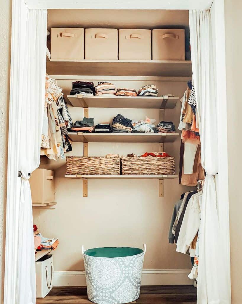 Organized closet with shelves, storage boxes, baskets, and hanging clothes; an empty decorative laundry basket sits on the floor