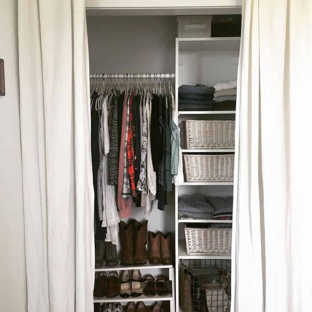 Closet with curtains open, showing clothes on hangers, stacked folded clothes, and shoes below. Baskets are on the shelves