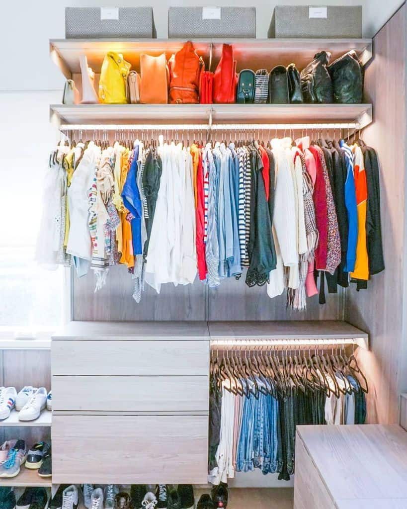 Neatly organized closet with colorful clothes on hangers, shoes on shelves, pants folded, and bags on top