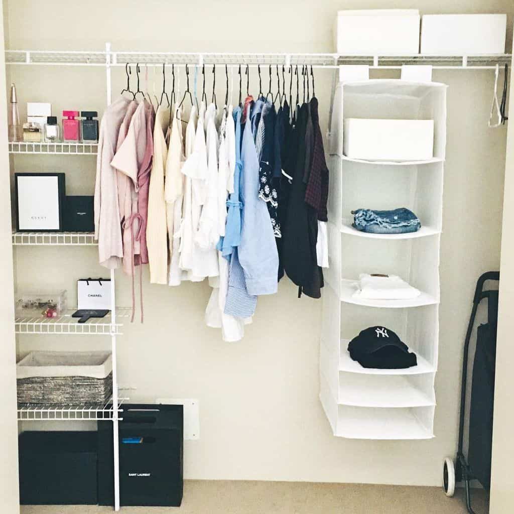 A tidy closet with neatly hung clothes, foldable shelves holding jeans and a cap, and boxes for storage on a beige wall