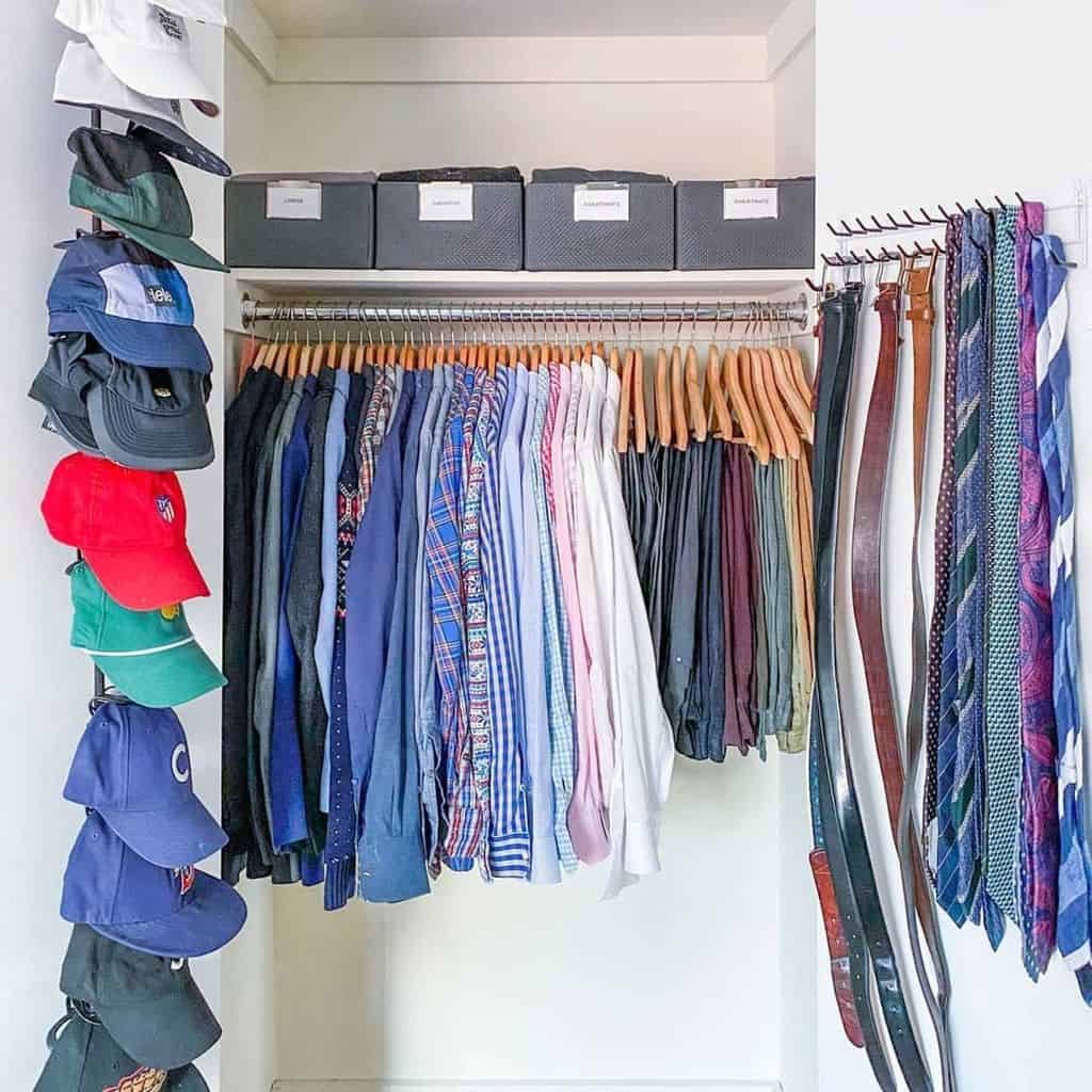 Closet with neatly arranged shirts on hangers, hats on the left, belts on the right, and storage boxes above