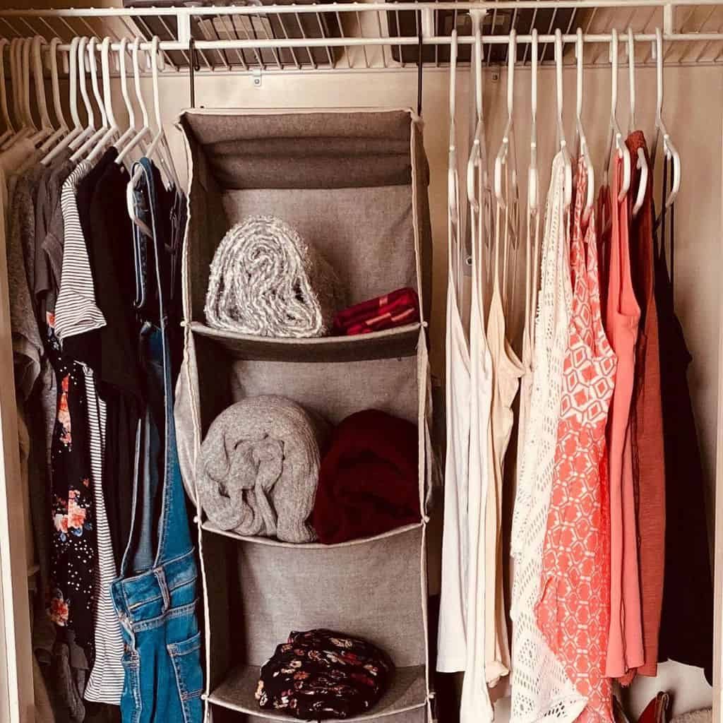 Organized closet with hanging clothes in various colors and a fabric shelf unit holding folded clothes and a scarf