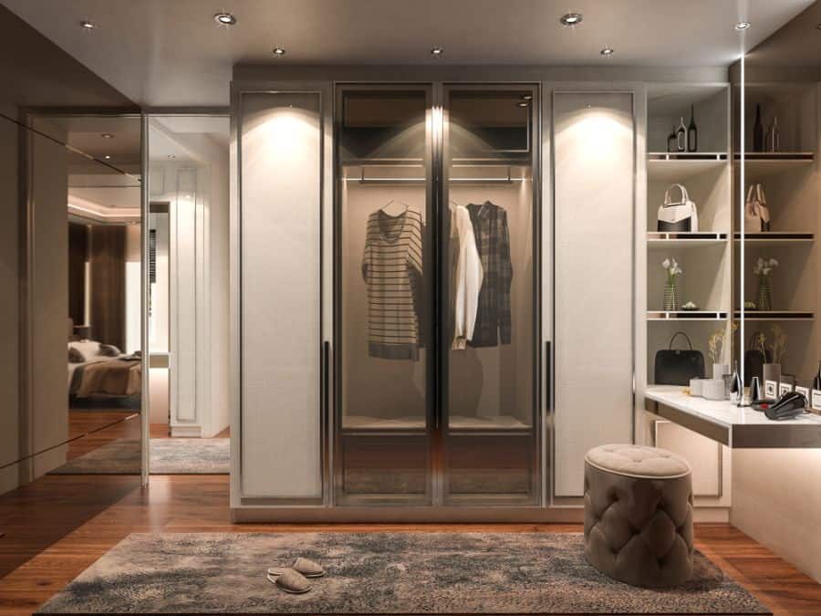 Luxurious walk-in closet with mirrored wardrobes, a rug, round stool, shelves with bags, and a lit dressing area