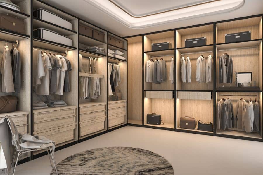 A spacious, modern walk-in closet with wooden shelves and racks of neatly hung clothes and suitcases, featuring accent lighting