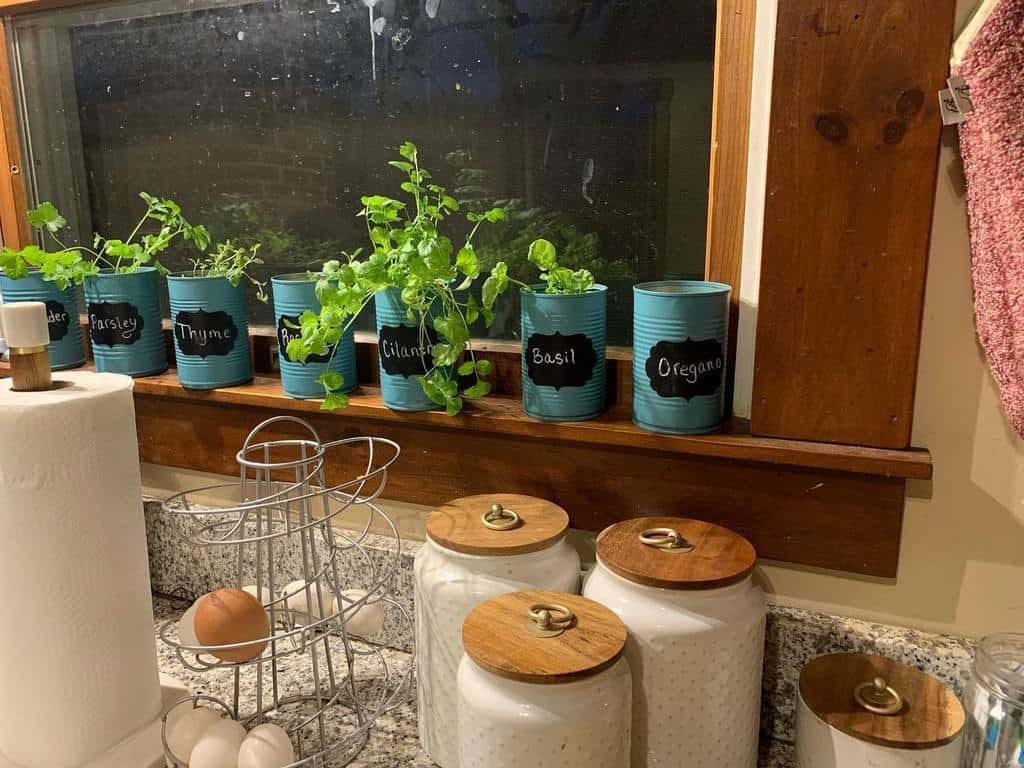 Kitchen windowsill with potted herbs labeled parsley, thyme, cilantro, basil, and oregano in blue cans