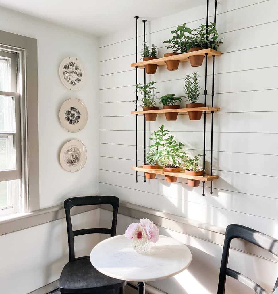 Wall-mounted herb garden with tiered wooden shelves and terracotta pots, adding greenery to a cozy dining nook with black chairs