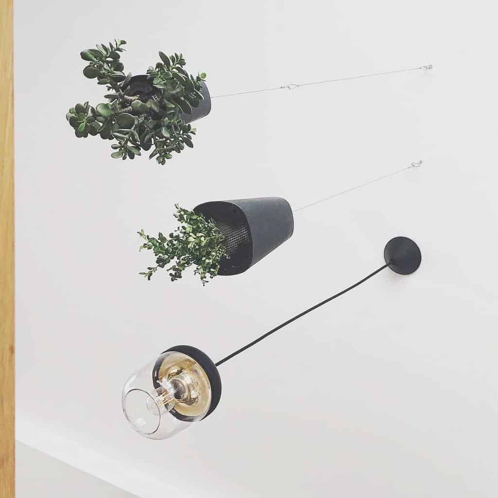 Two black planters with green plants and a modern wall-mounted lamp hanging on a white wall