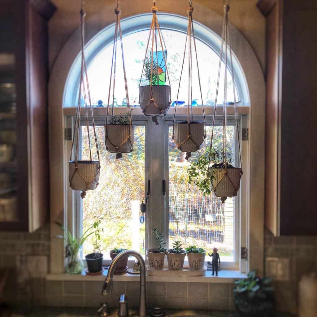 Kitchen window herb garden with macrame-hanging planters and potted plants on the sill, creating a cozy and functional indoor space