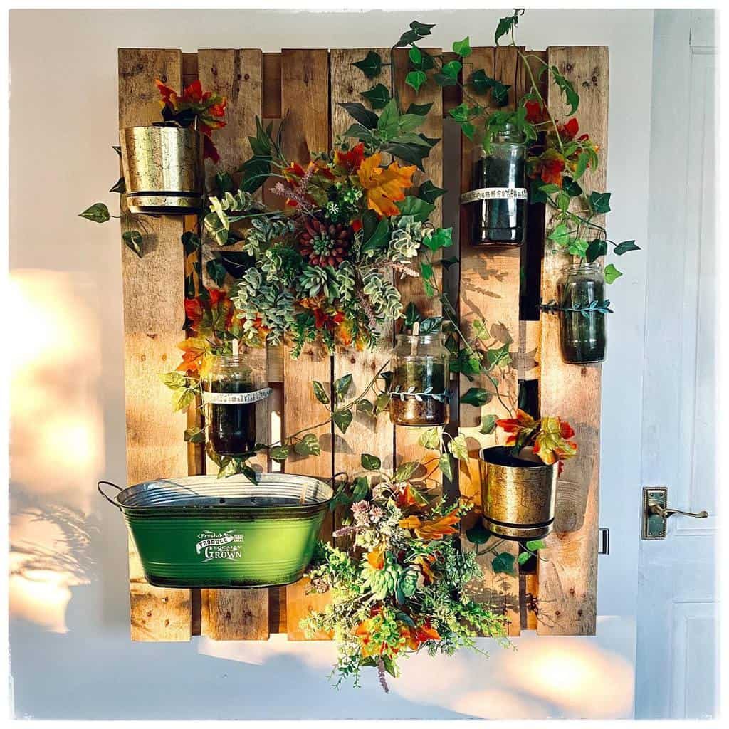 Vertical wooden pallet wall decor with hanging plants, metallic pots, and a green container, adorned with autumn leaves and vines