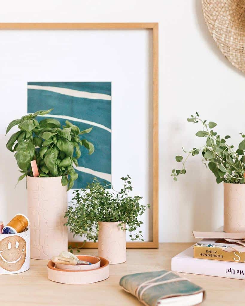 Three potted plants on a wooden table with books and a framed abstract art piece in the background