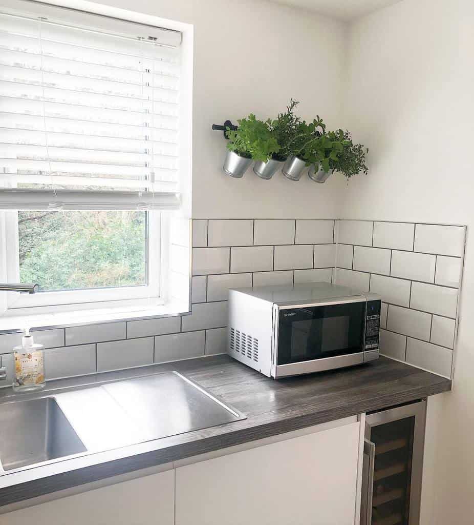 Minimalist kitchen with a wall-mounted herb garden in metal pots, adding fresh greenery above a modern tiled backsplash