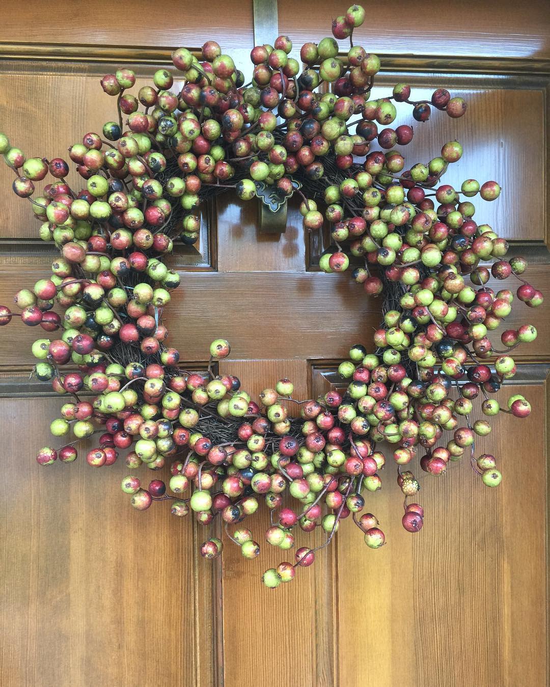 A wreath made of small red and green berries hangs on a wooden door