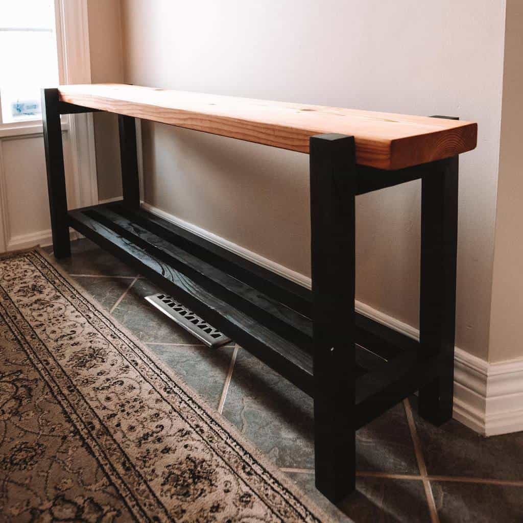 A wooden console table with a light brown top and black legs is positioned against a wall on a patterned rug