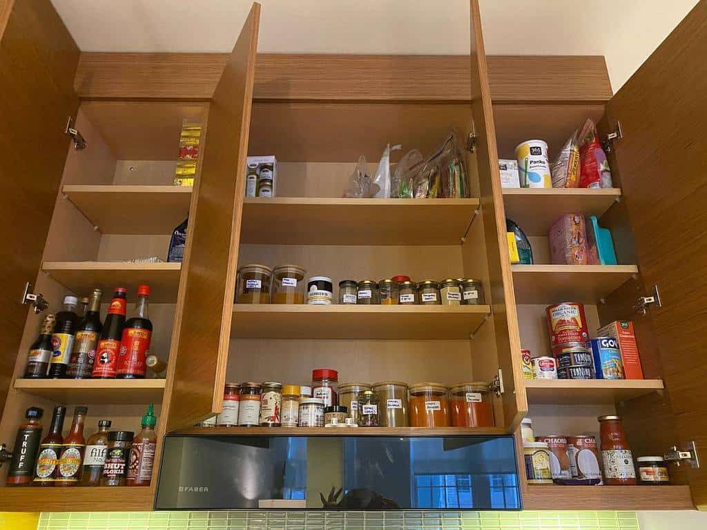 Open kitchen cabinets filled with various spices, jars, and food items, with a range hood visible below the middle cabinet