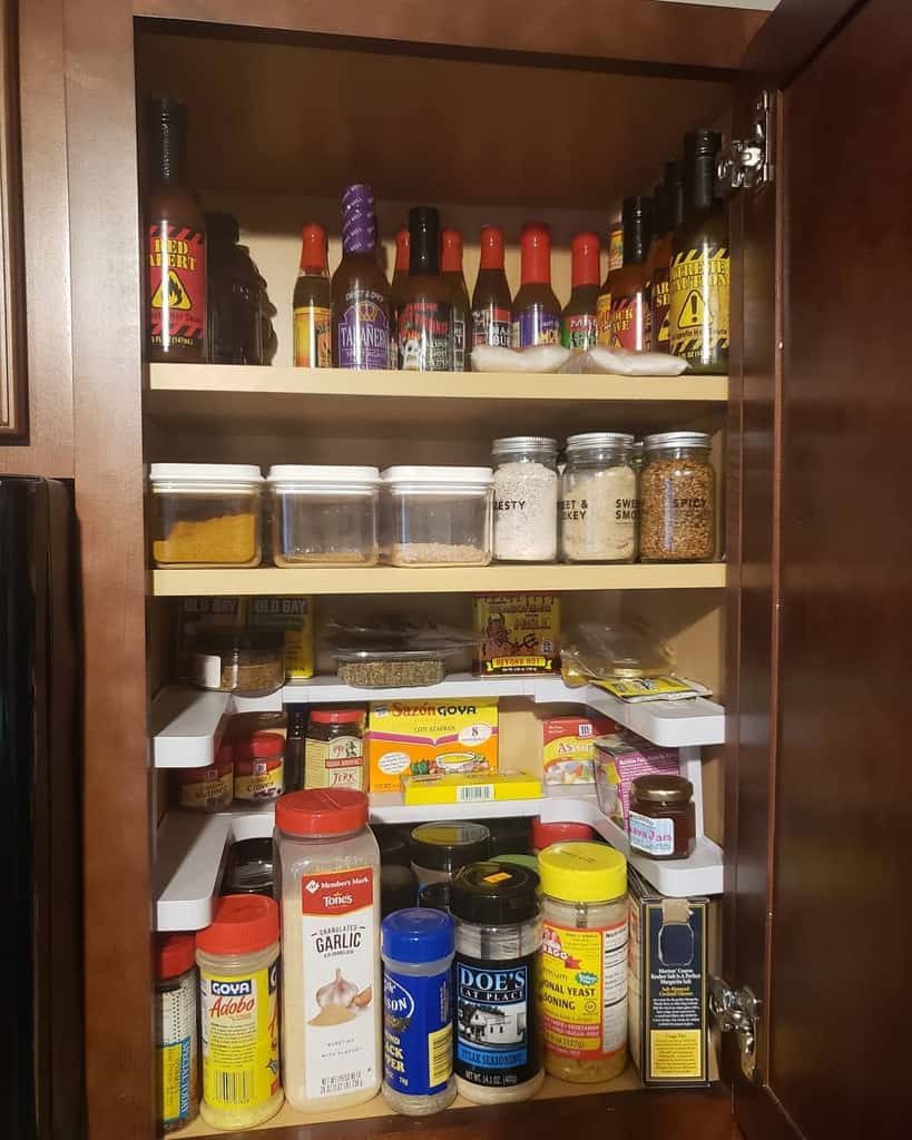 A kitchen cabinet filled with various spices, seasonings, and hot sauces organized on shelves