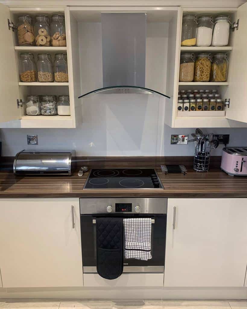 Modern kitchen with neatly organized glass jars storing spices, pasta, and baking essentials inside open cabinets for a clean, functional look