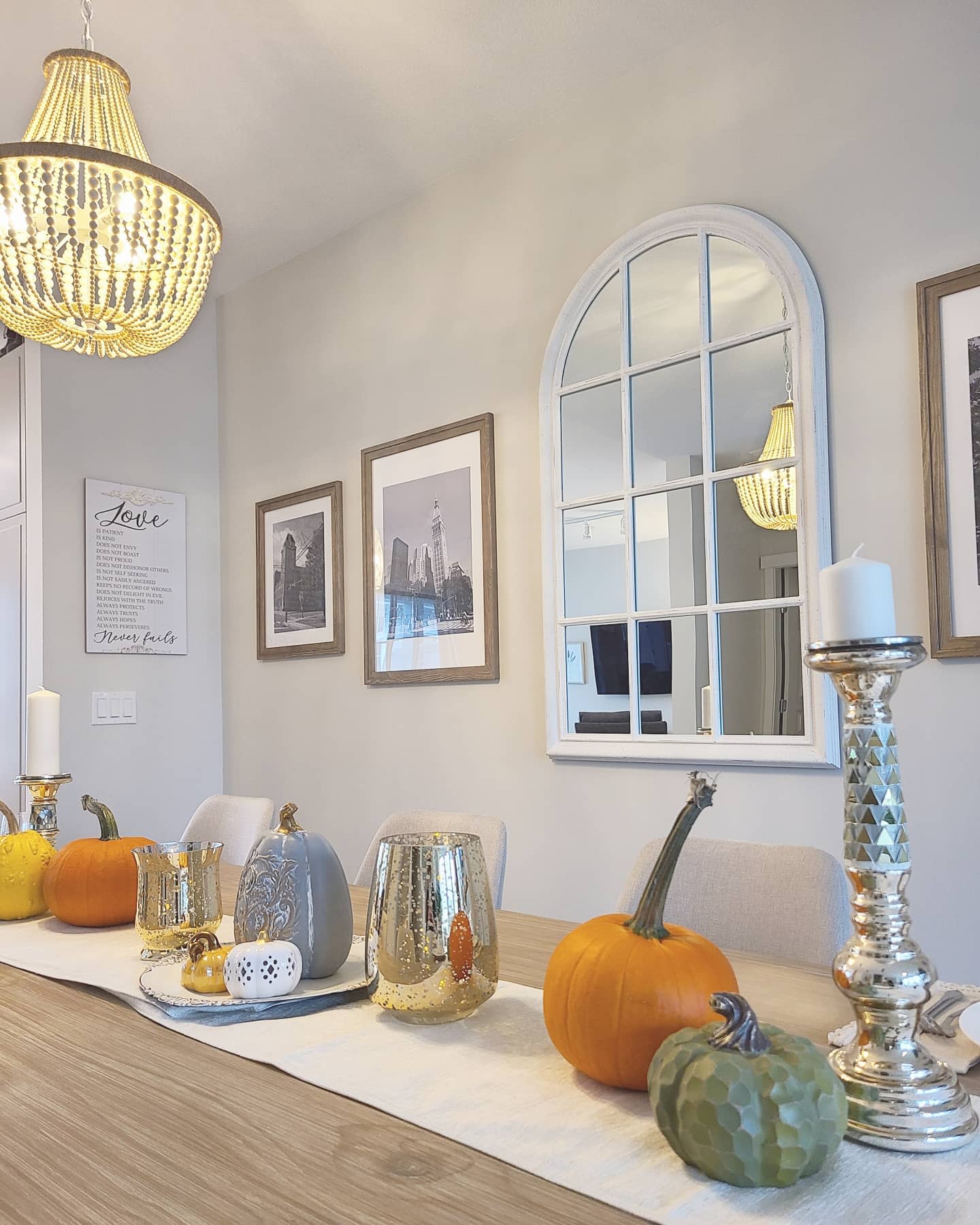 Elegant fall dining table centerpiece with pumpkins, gold accents, and candle holders, set in a bright and modern space