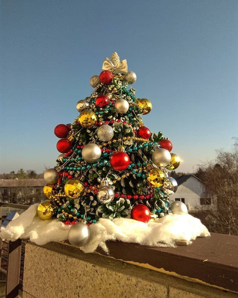 Miniature Christmas tree with colorful ornaments and snow on a ledge, set against a clear blue sky