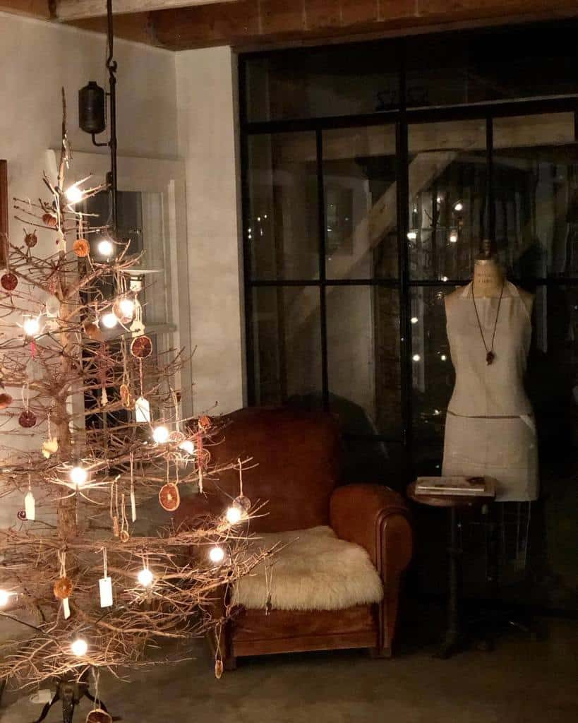 Cozy room with a lit Christmas tree, a leather chair with a fur throw, and a dress form by a large window