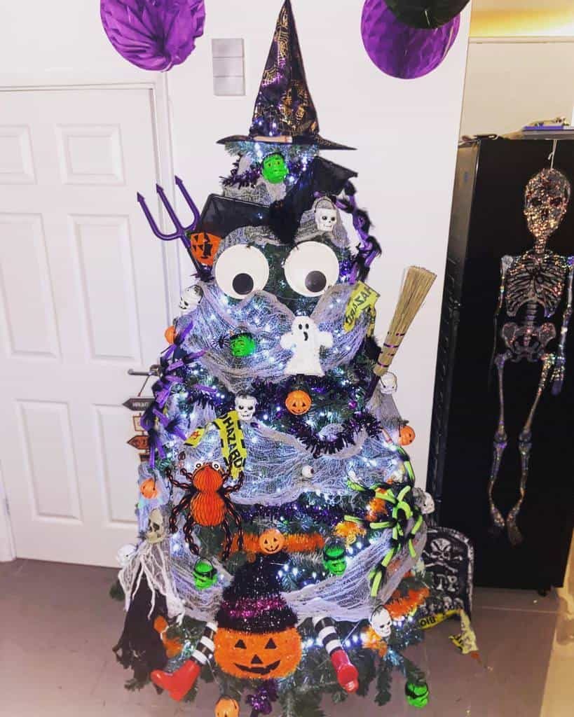 A Halloween-themed tree decorated with witches' hats, googly eyes, skeletons, spiders, and pumpkins, with purple and green accents