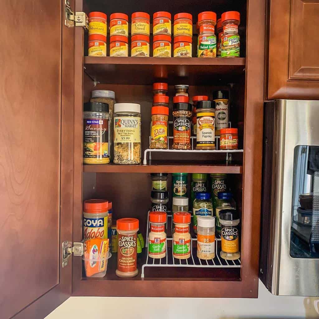 A wooden cabinet filled with neatly arranged spice jars, organized by type and size on three shelves