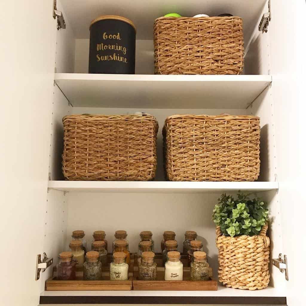 Neatly organized cupboard with woven baskets and a wooden spice rack holding cork-topped glass jars, creating a tidy and stylish kitchen space