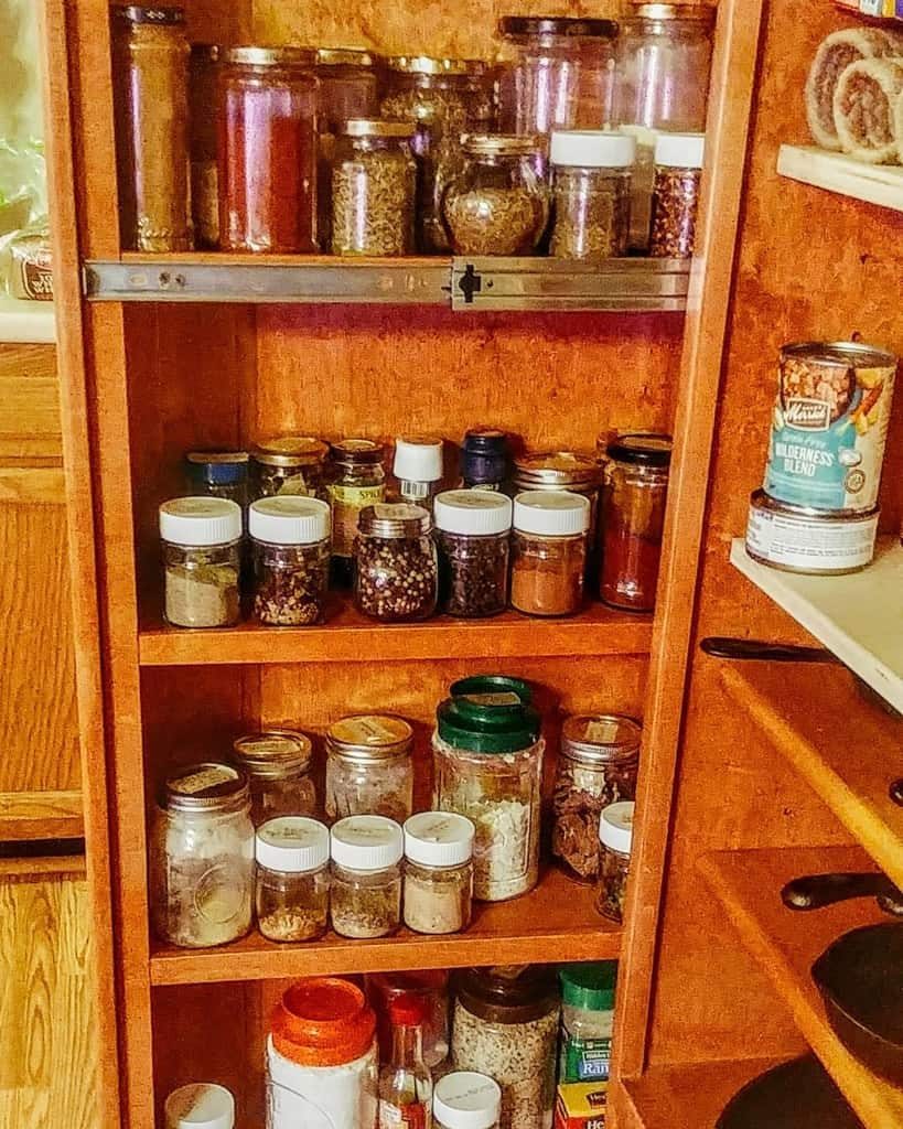 Wooden spice rack filled with various jars of spices and herbs, a can and a jar are on the adjacent countertop