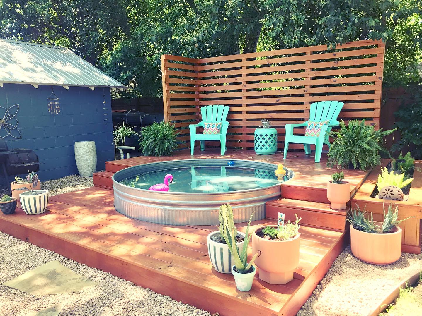 Backyard with a small above-ground pool, two turquoise chairs, and various potted plants on a wooden deck with privacy screen