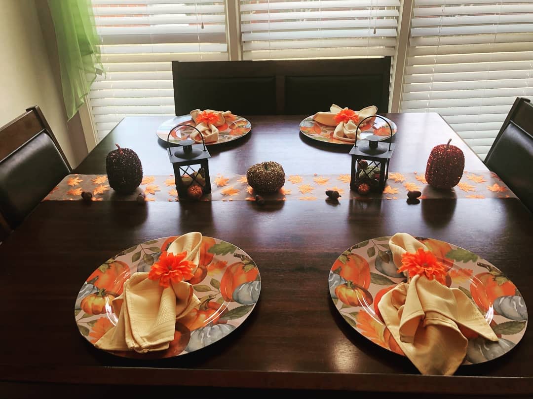 A fall-themed table setting with pumpkin-patterned plates, orange flowers, lanterns, and decorative pumpkins on a dark wooden table