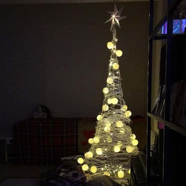 Minimalist Christmas tree made of string lights with glowing bulbs and a star on top, set in a dimly lit room