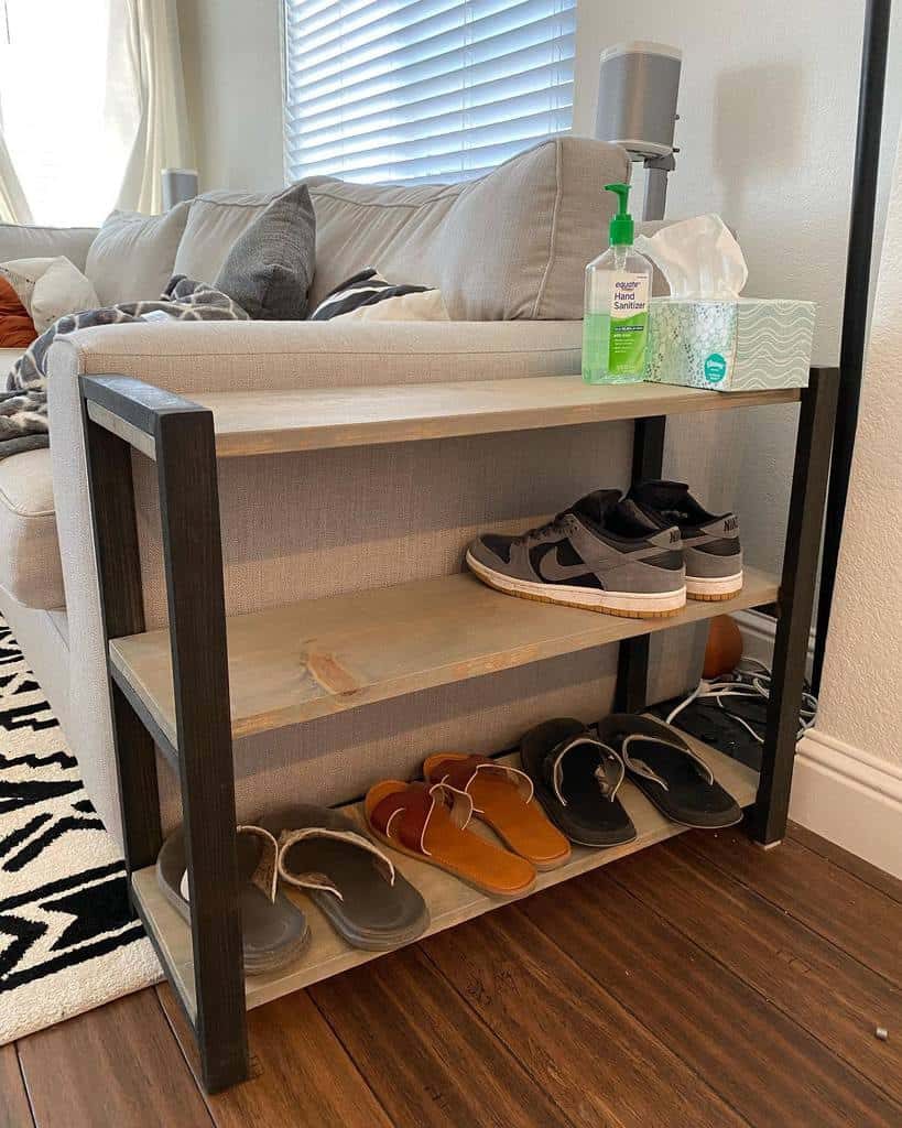 Rustic shoe storage rack with metal and wood shelves placed beside a sofa, neatly organizing sneakers and sandals in a cozy living space