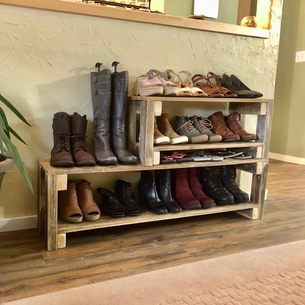 Wooden shoe rack with various boots, shoes, and sandals neatly arranged on three shelves in a room with wooden flooring