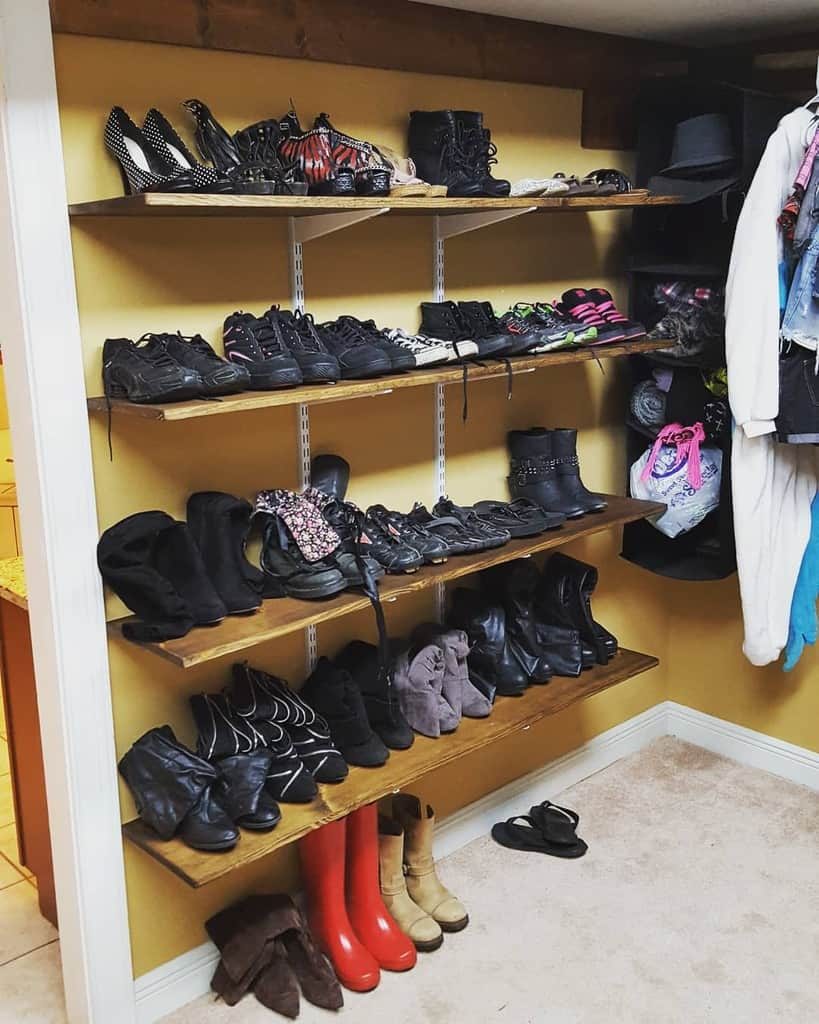 A collection of shoes arranged on wooden shelves, featuring various types including boots, heels, and red rain boots in a closet