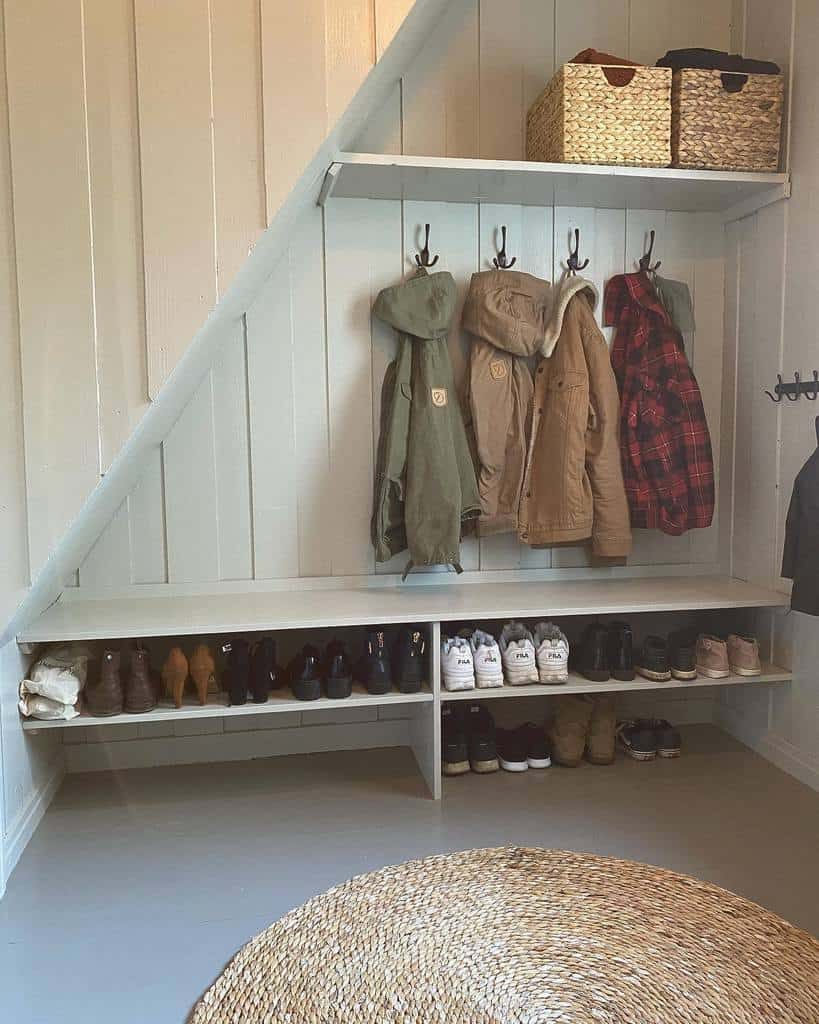 Built-in shoe storage under a bench in a mudroom with coat hooks, woven baskets, and an organized under-stairs space