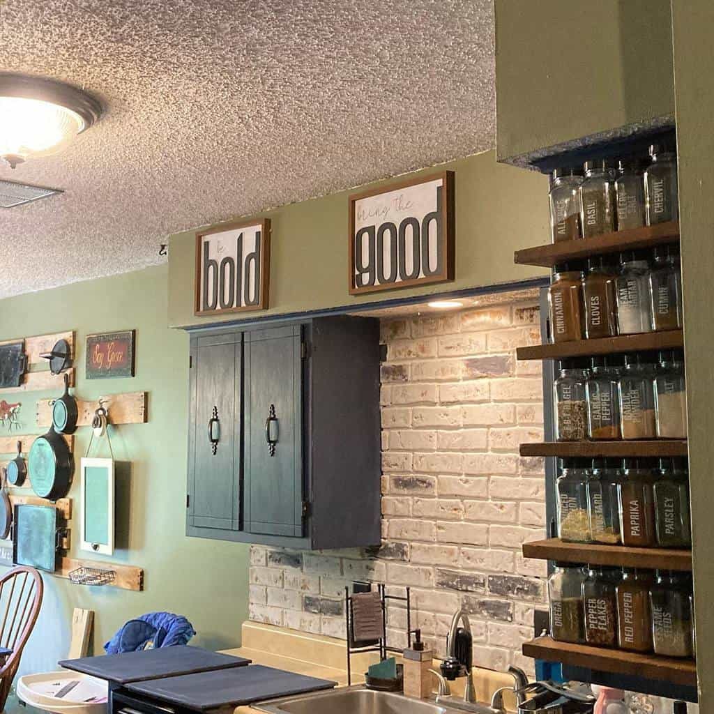 Built-in wooden spice rack with labeled glass jars, neatly arranged beside a rustic kitchen with green walls and black cabinetry