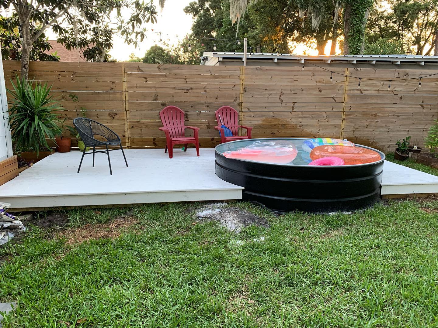 Backyard with a deck, two chairs, and a small round above-ground pool surrounded by green grass