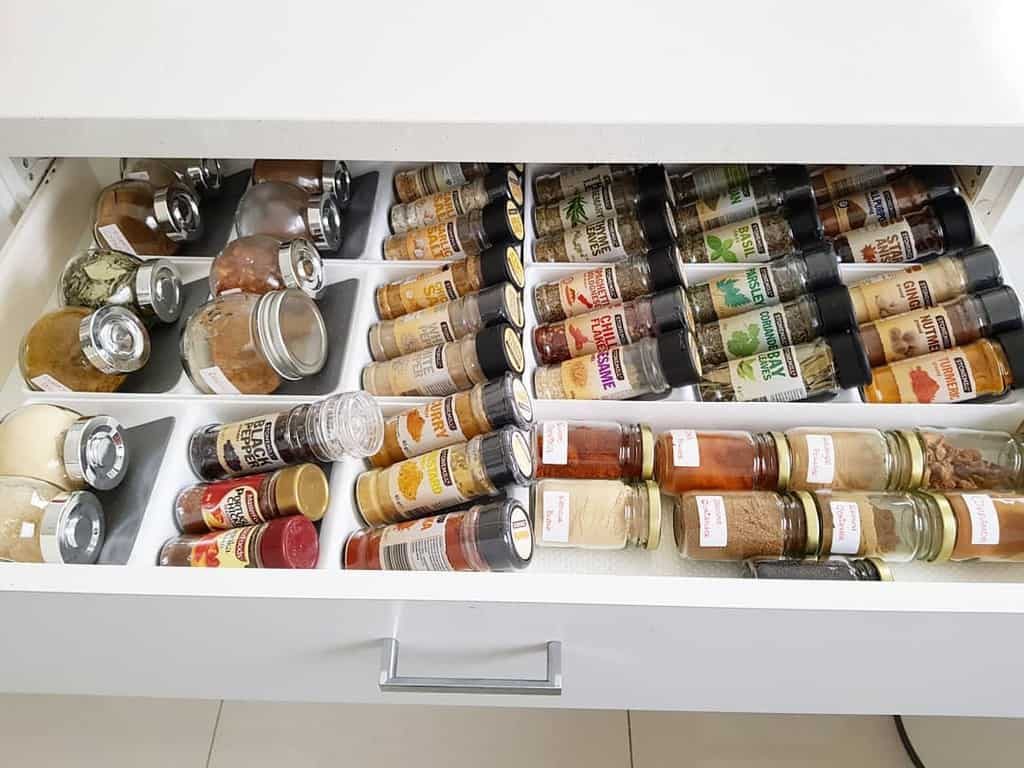 Drawer filled with neatly organized spice jars and containers, labeled and arranged in rows