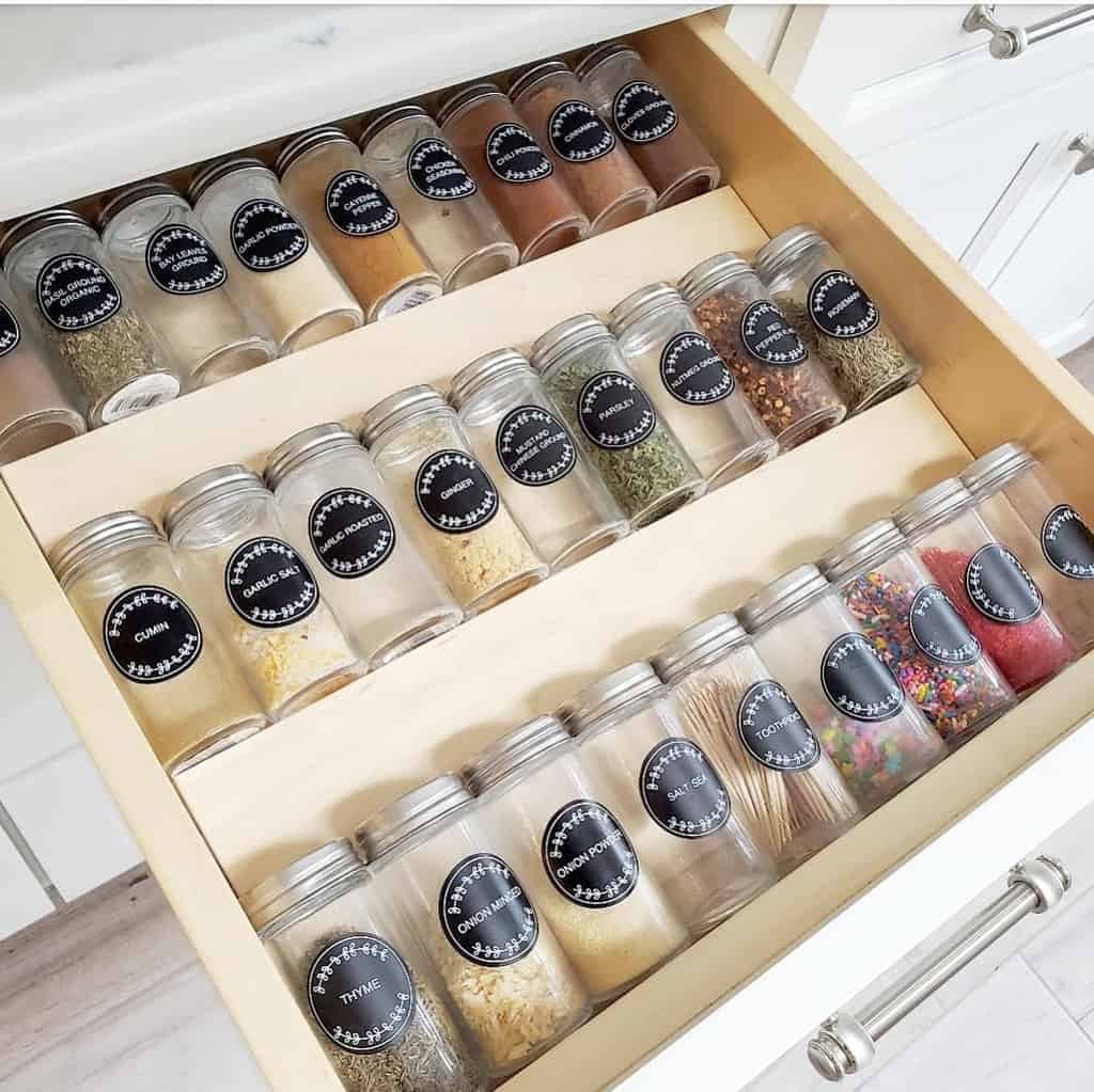 Open drawer with neatly organized spice jars, each jar has a black label with white text naming the contents