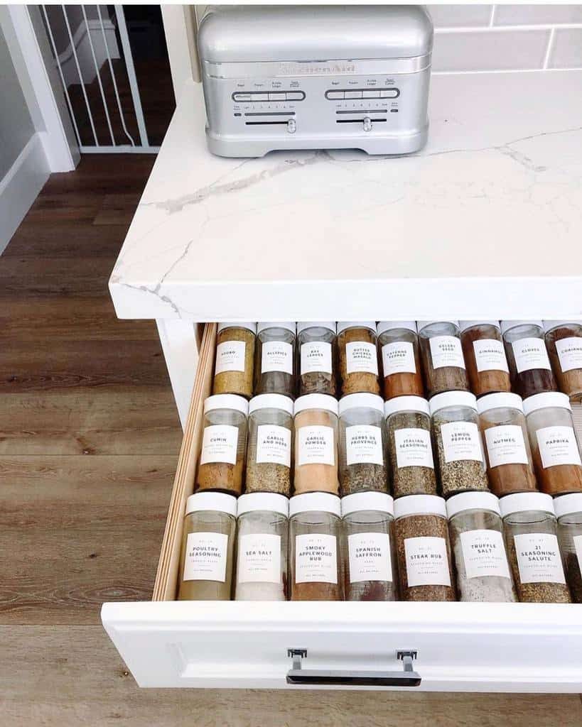 Open kitchen drawer with neatly organized labeled spice jars in two rows; silver toaster on the countertop above