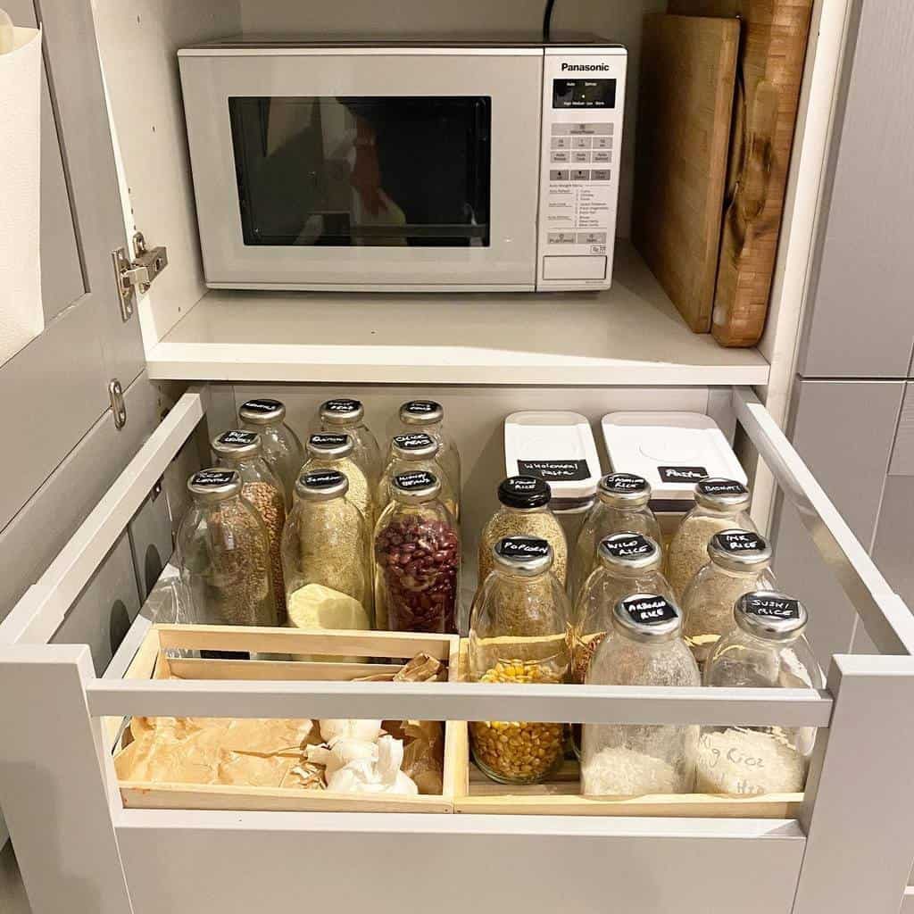 Kitchen drawer with glass jars of spices and grains, two labeled containers, and a microwave above