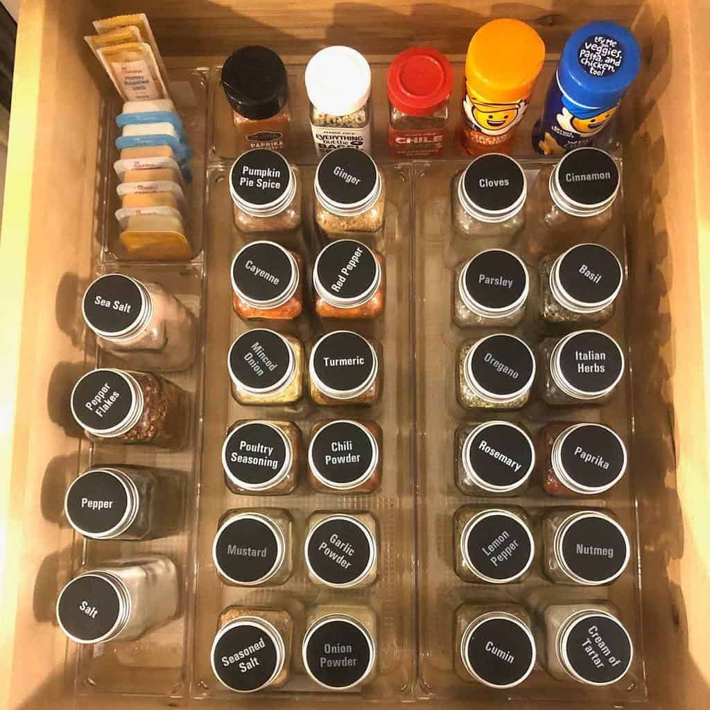 Organized drawer with labeled spice jars and packets of seasoning, including sea salt, pumpkin pie spice, and Italian herbs