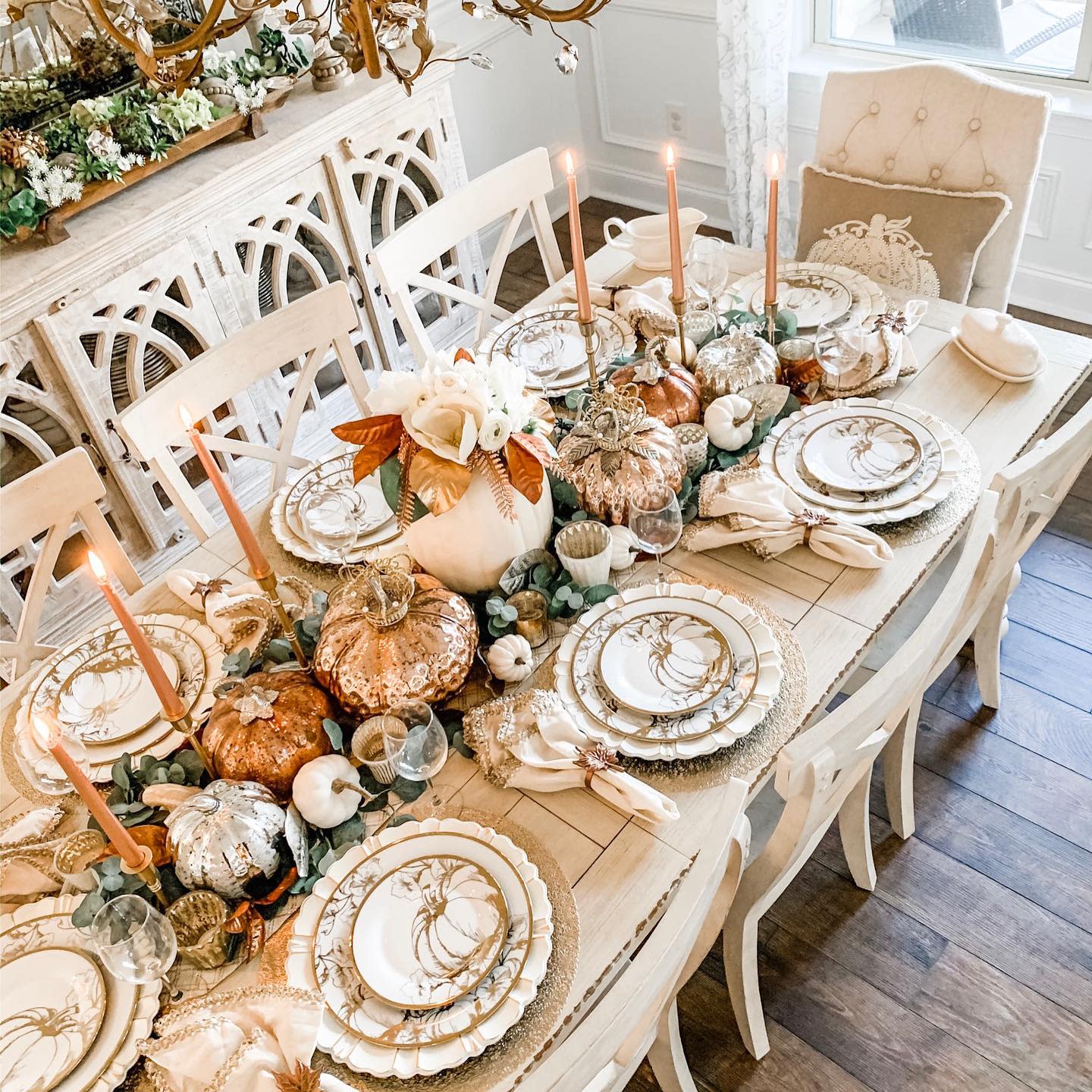 Elegant fall-themed dining table with pumpkins, candles, and decorative plates arranged on a white wooden table