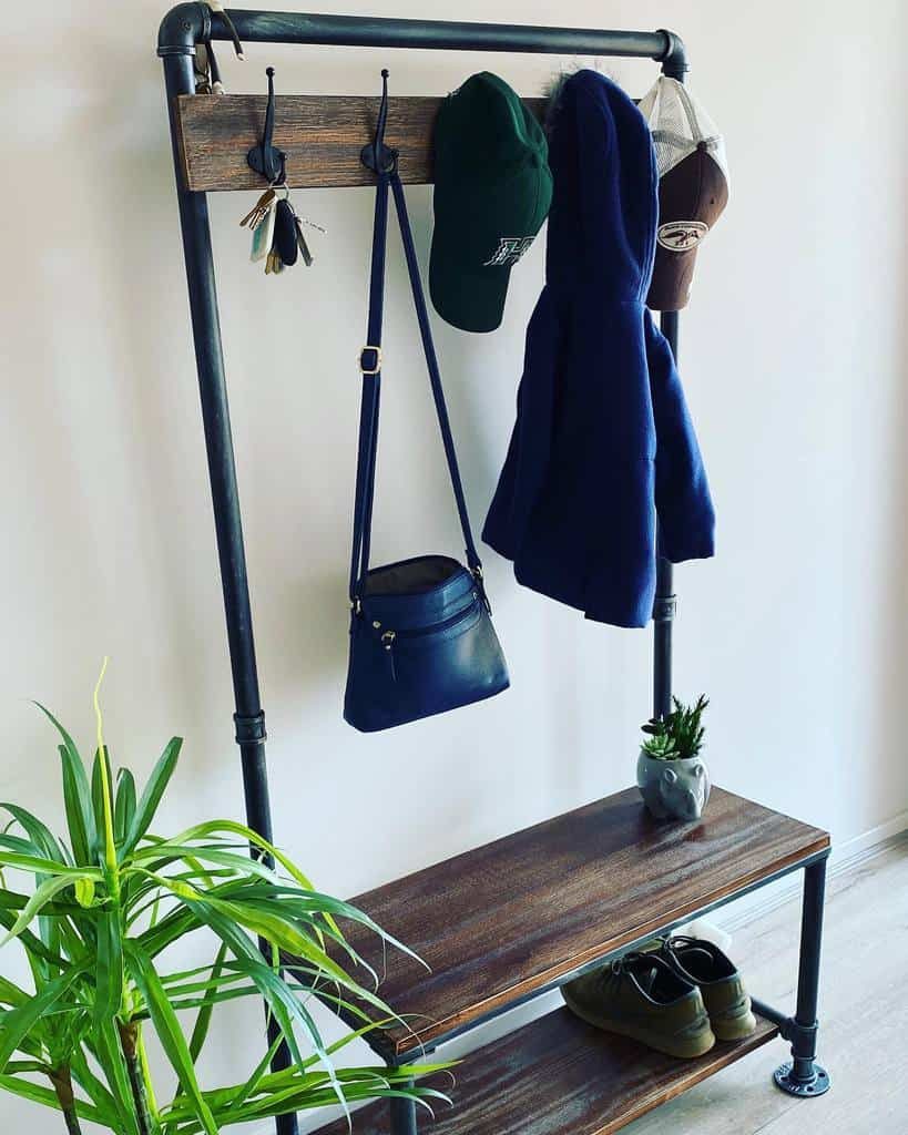 Wall-mounted industrial coat rack with hats, keys, coat, purse hanging; bottom shelf holds shoes and a small plant