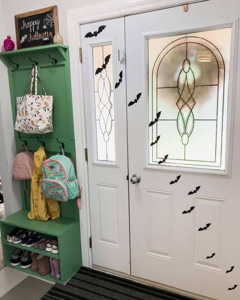 Green entryway storage bench with hooks for bags and coats, built-in shoe shelves, and Halloween bat decorations on the front door